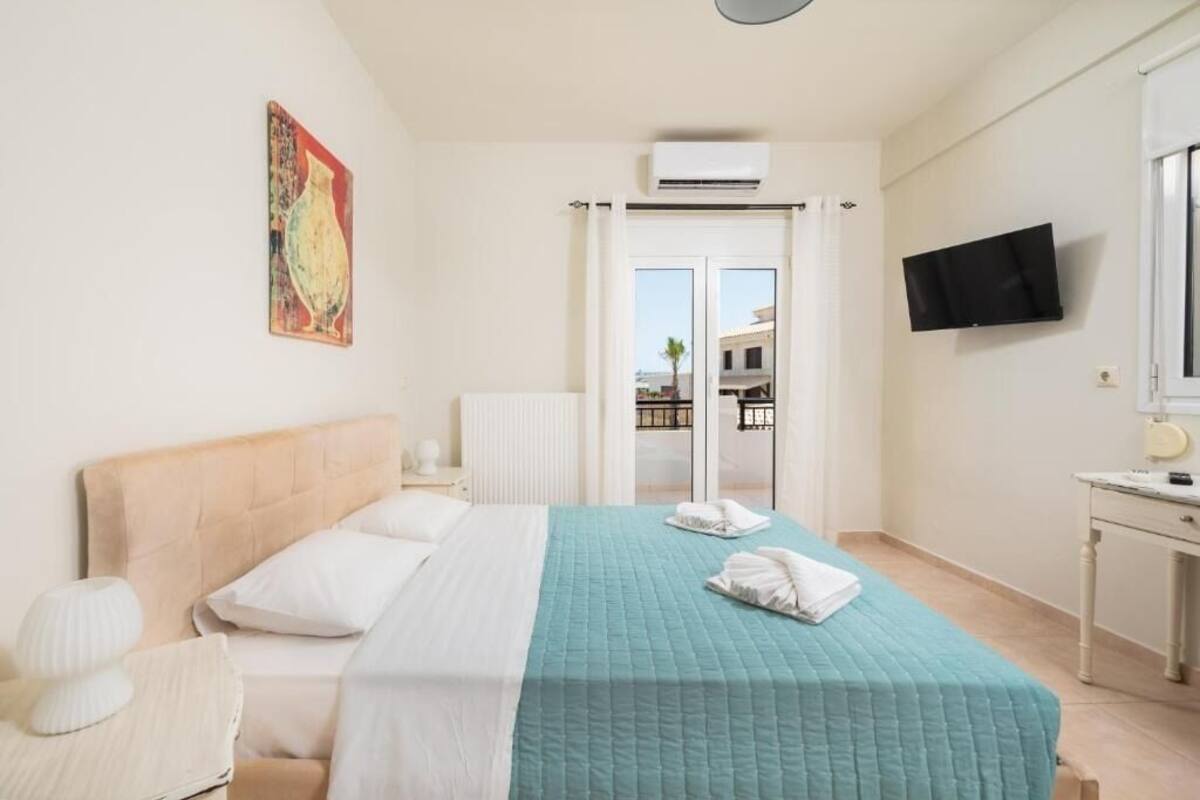 A hotel room with a bed, a desk, a TV, and a window with a view of buildings.