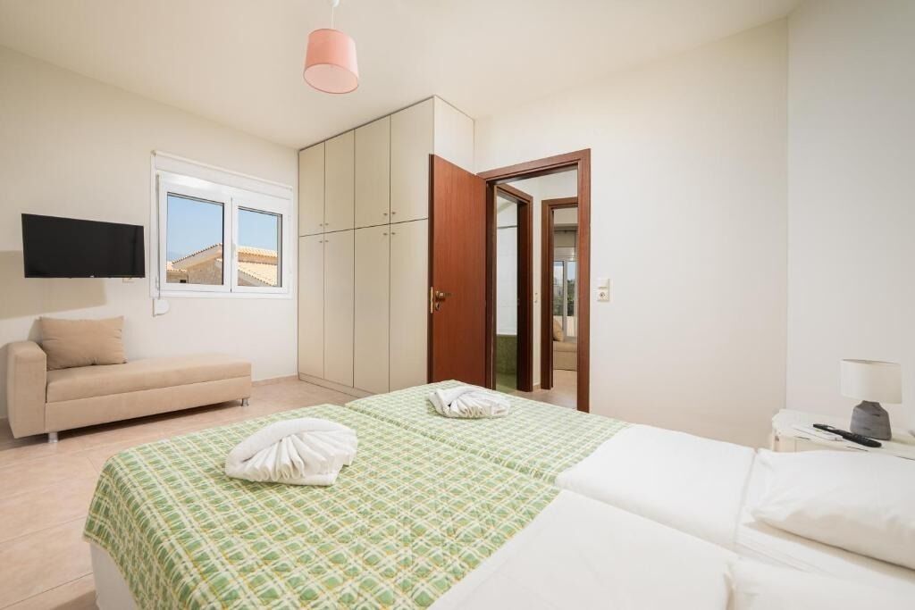 Un dormitori amb llit, sofà, armari, televisió i una porta que dona a una altra habitació.