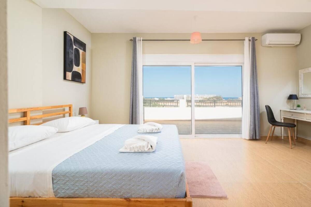 A hotel room with a bed, a desk, a chair, a window with a view, and an air conditioning unit.