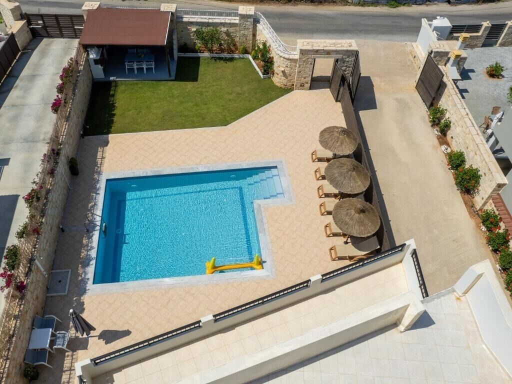 Una piscina con terraza solárium, sillas de descanso y un pequeño edificio con techo rojo.