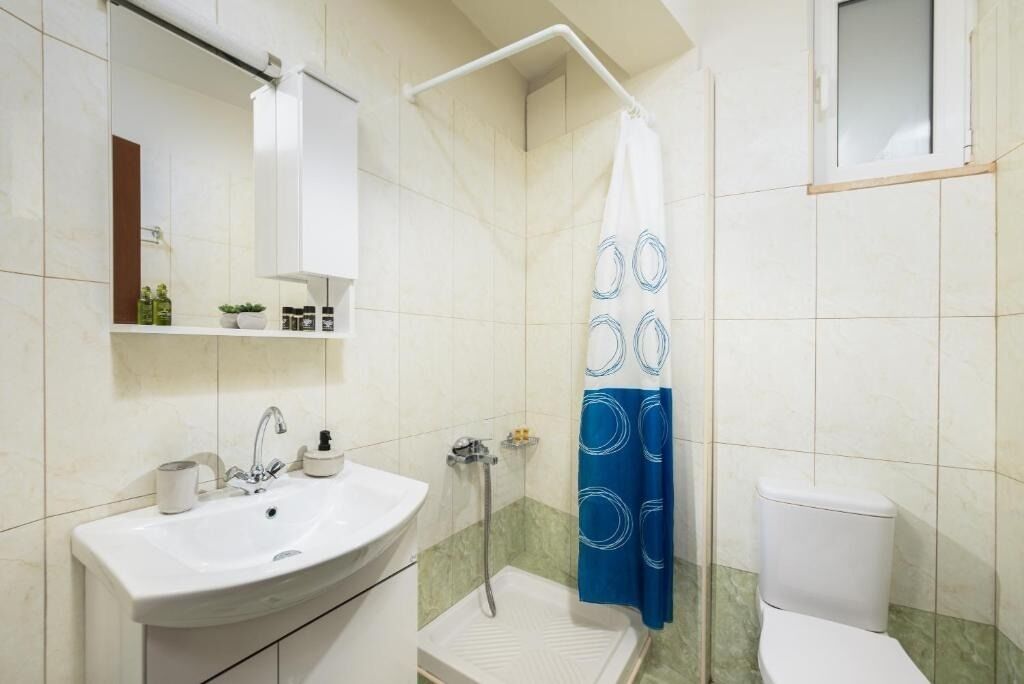 Een badkamer met een wit wastafel, spiegel en toilet. Er is een douche met een blauw-witte douchegordijn.