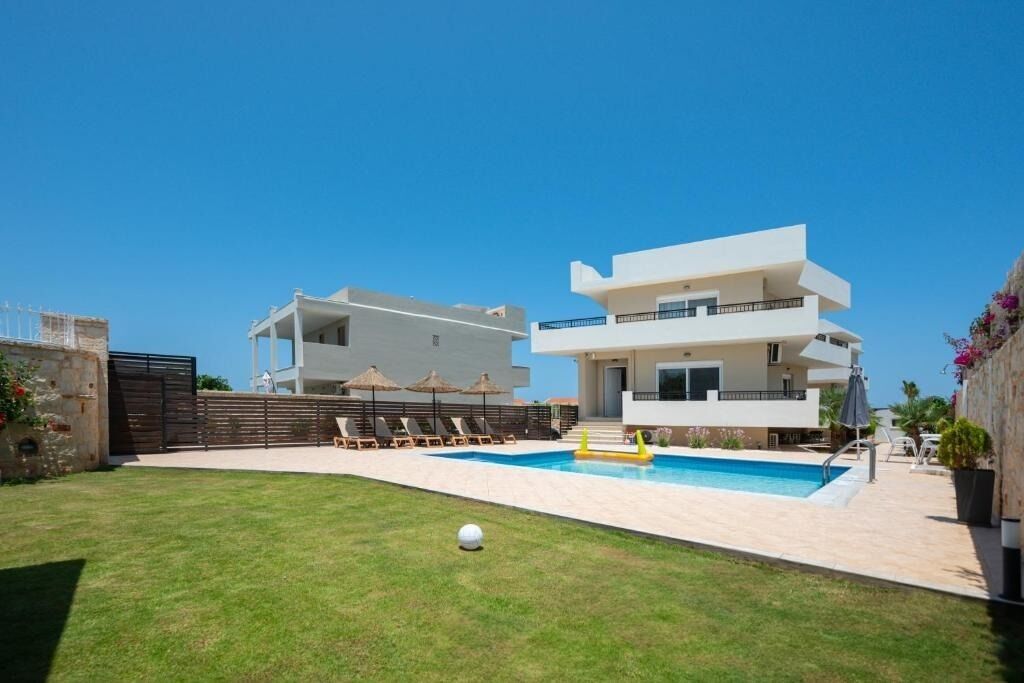 A modern two-story building with a swimming pool, outdoor seating, and a well-maintained lawn.