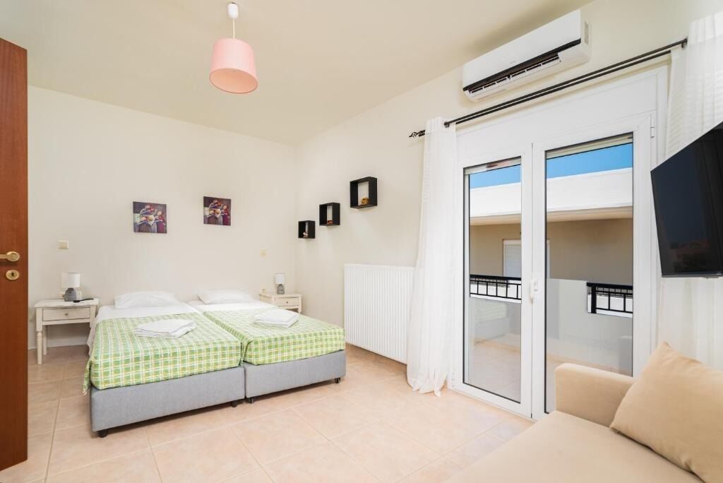 A bedroom with two beds, a sofa, a TV, and a balcony with a view.