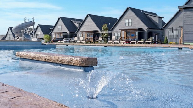 Un área de piscina con fuente de agua, sillas de descanso y una fila de casas con techo inclinado.