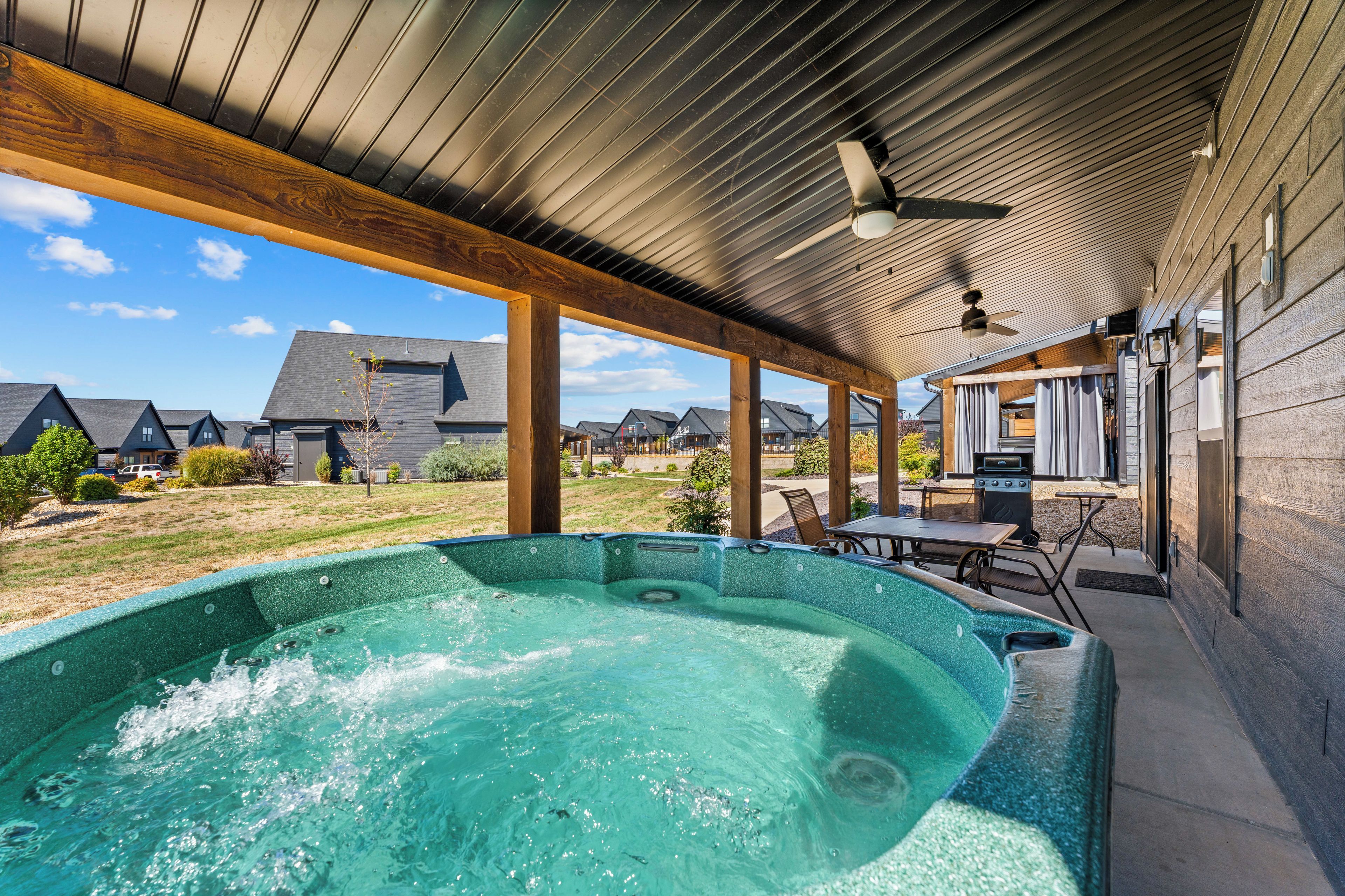 A hot tub area with a covered patio, outdoor seating, and a view of neighboring houses.
