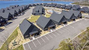 Una hilera de cabañas modernas con techos oscuros, un estacionamiento y vistas al lago.