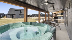 Un espacio al aire libre techado con un jacuzzi, vigas de madera y un patio con una parrilla.