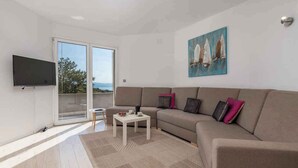 A modern living room with a sofa, a coffee table, and a TV. There is a painting on the wall and a view through the glass door. - Holiday home with terrace and pool (Poljane)