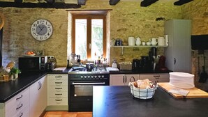 Una cocina rústica con pared de piedra, vigas de madera, un reloj grande y electrodomésticos básicos.