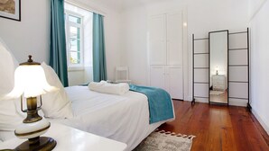 Un dormitorio con cama, una mesita de noche con lámpara, ventana con cortinas, armario y espejo.