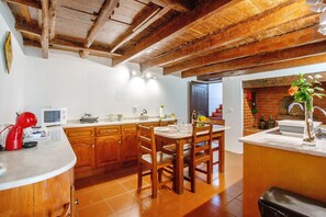 A kitchen with wooden cabinets, a dining table, and a brick fireplace. - Holiday Home 'Mother's House' with Sea View, Private Terrace and Wi-Fi (Calheta)