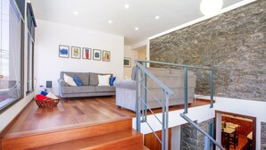 Una sala de estar moderna con una escalera, suelo de madera, un sofá gris y una pared de acento de piedra.
