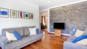 Una sala de estar con un sofá gris, un televisor de pantalla plana y una pared de piedra.