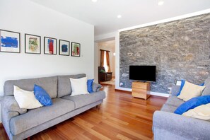 A living room with a grey sofa, a flat-screen TV, and a stone wall.