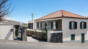 Un edificio de dos pisos con fachada de piedra, contraventanas verdes y techo de tejas rojas.