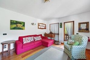 En stue med en rød sofa, en grøn lænestol med mønster, et træbord, et billede på væggen og et vindue med gardiner.