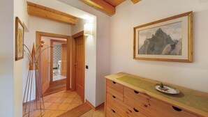 A hallway with wooden beams, a wooden dresser, a framed painting, and a floor lamp. - Apartment 'Villa Cleila Blu D' with Mountain View, Shared Garden and Balcony (San Vito di Cadore)