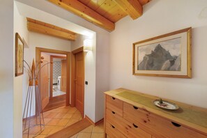 A hallway with wooden beams, a wooden dresser, a framed painting, and a floor lamp.