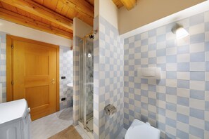 A bathroom with a checkered tile wall, a wooden door, a glass shower enclosure, and a white sink. - Apartment 'Villa Cleila Blu D' with Mountain View, Shared Garden and Balcony (San Vito di Cadore)