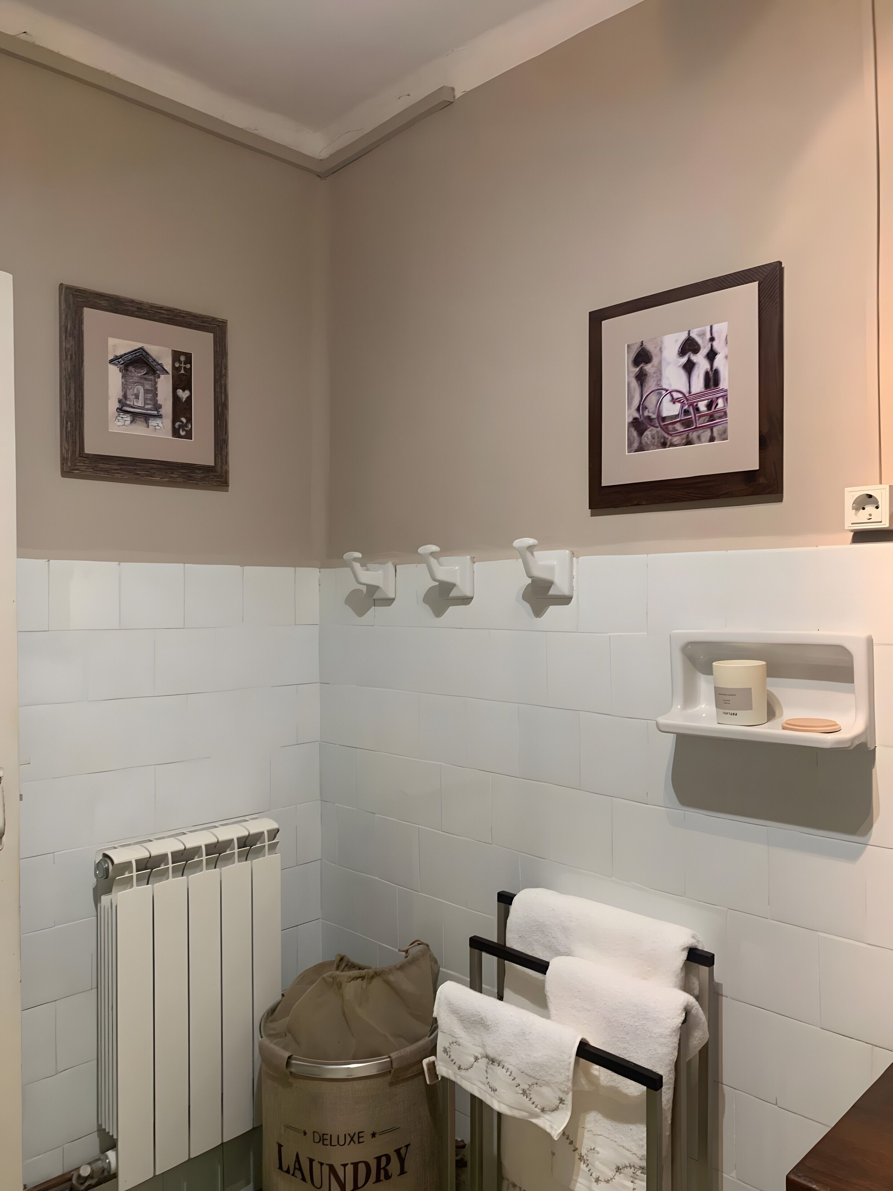 Un baño con un radiador, una bolsa para la ropa, un perchero y dos cuadros en la pared.