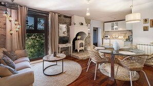 Un salón acogedor con un sofá, una mesa redonda, sillas de mimbre, una chimenea y una cocina al fondo.