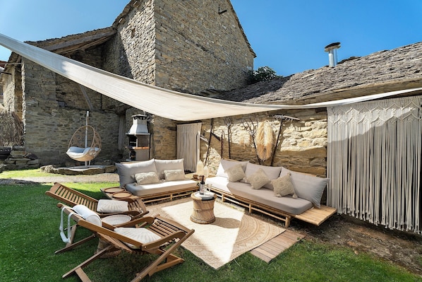 A stone building with a stone wall, a hanging chair, a sofa set, and a swing.