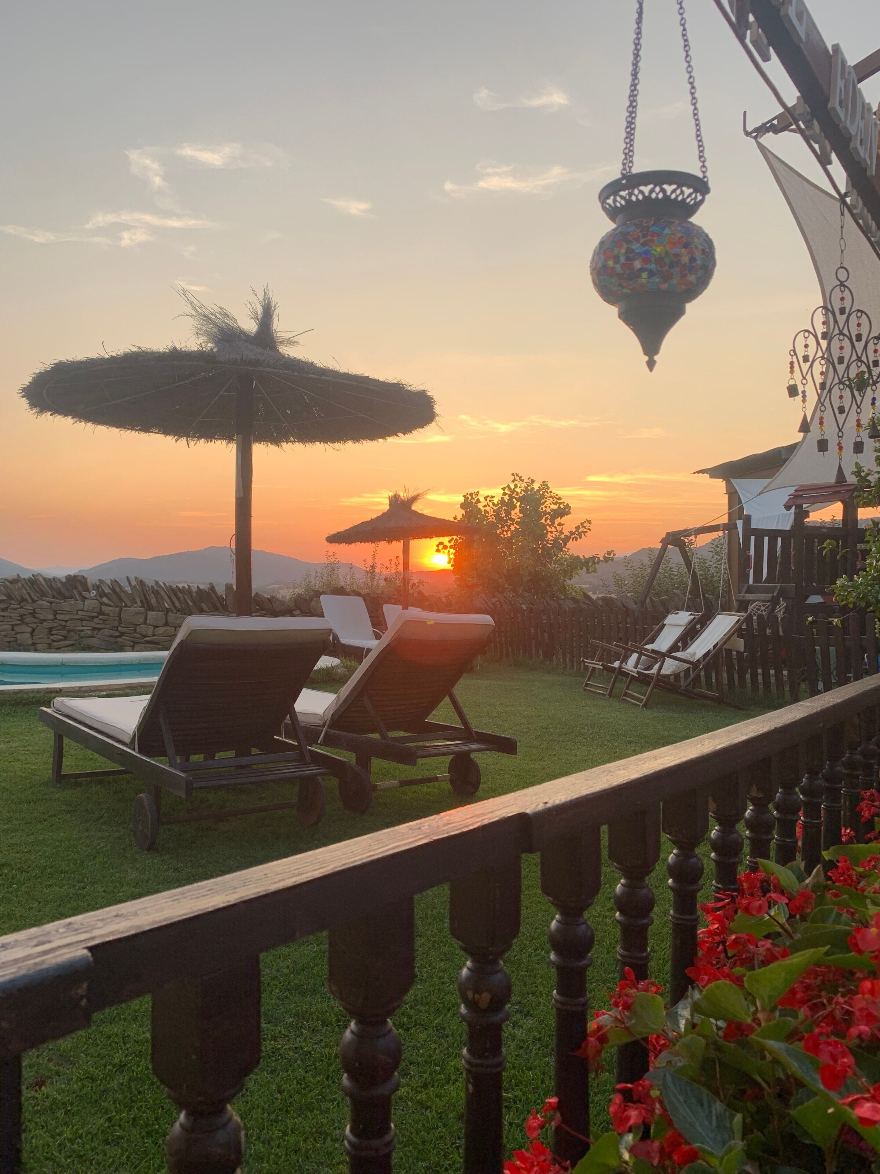 A sunset view with lounge chairs, a pool, and a decorative hanging lantern.