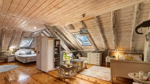 Un dormitorio acogedor en el ático, con vigas de madera, tragaluces, una mecedora, una cama y un aparador.