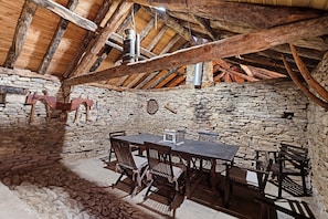A rustic stone-walled room with a wooden table and chairs, a stone fireplace, and a sloped wooden ceiling.