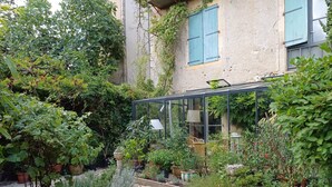 A greenhouse with plants and a table, surrounded by a gravel path. - Le Tonnelier – Charming House with Pool in the Heart of Quercy (Limogne-en-Quercy)