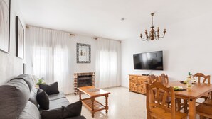 Een woonkamer met een bank, een houten eettafel, stoelen, een televisie, een open haard en een kroonluchter.