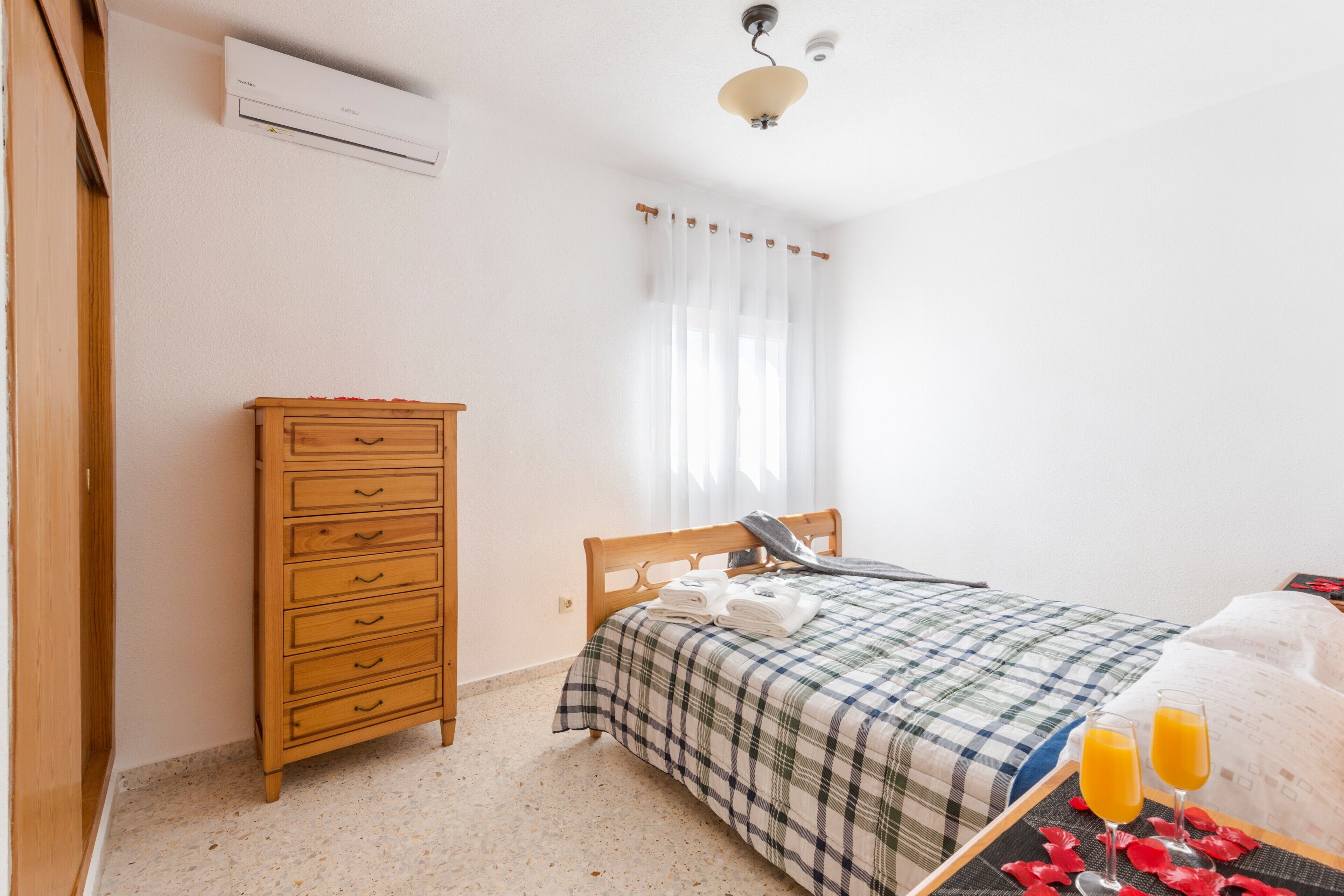 A bedroom with a bed, a wooden dresser, an air conditioner, and a window with curtains.