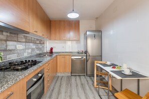 A modern kitchen with wooden cabinets, a stainless steel refrigerator, a gas stove, and a dining area with a table and chairs.