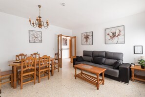 A living room with a sofa, wooden dining table, chairs, a chandelier, and framed floral artwork on the walls.