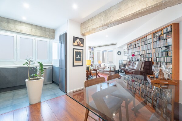 Un vaste espace de vie comprenant une grande table en verre, une bibliothèque remplie de livres et une plante en pot.