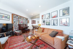 Un salon comprenant un canapé, une table basse, un téléviseur, une bibliothèque et des œuvres d’art accrochées aux murs.