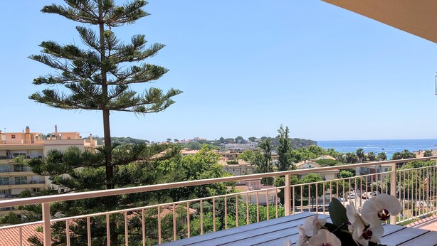 A balcony with a wooden table, white orchids, and a view of the sea and buildings. - Apartment 'Apartament Creu De Sant Pol' with Sea View and Wi-Fi (Sant Feliu de Guíxols)