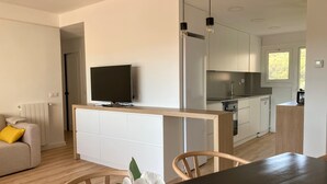 A modern kitchen with a built-in oven, a dining area with a table and chairs, and a TV mounted on a cabinet. - Apartment 'Apartament Creu De Sant Pol' with Sea View and Wi-Fi (Sant Feliu de Guíxols)