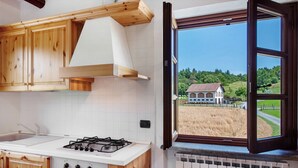 Una cocina con armarios de madera, una estufa a gas y vista a un paisaje rural por una ventana abierta.