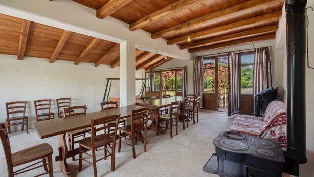 Un comedor con una larga mesa de madera y sillas, un sofá, y un estufa de leña.
