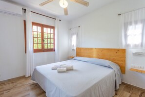 Une chambre à coucher avec une tête de lit en bois, un lit recouvert de draps blancs, un plancher en bois et une fenêtre avec des rideaux.