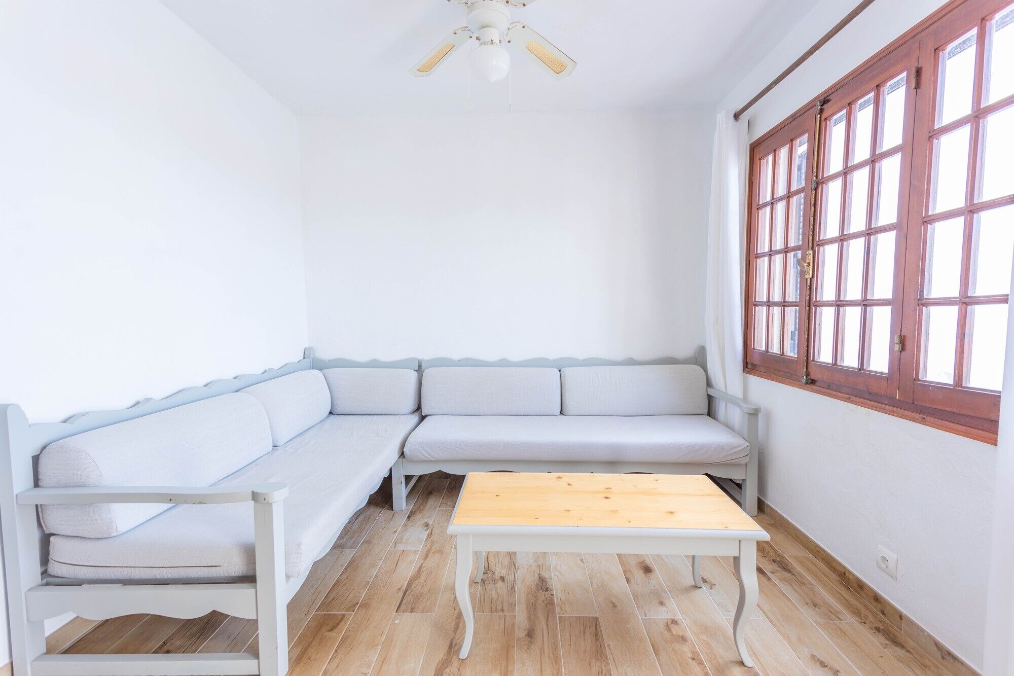 Ein Zimmer mit einer weißen Couch, einem Holztisch und einem Fenster mit Holzrahmen.