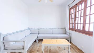 Ein Zimmer mit einer weißen Couch, einem Holztisch und einem Fenster mit Holzrahmen.