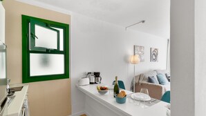 Una cocina moderna con encimera blanca, ventana con marco verde y comedor con mesa para dos.