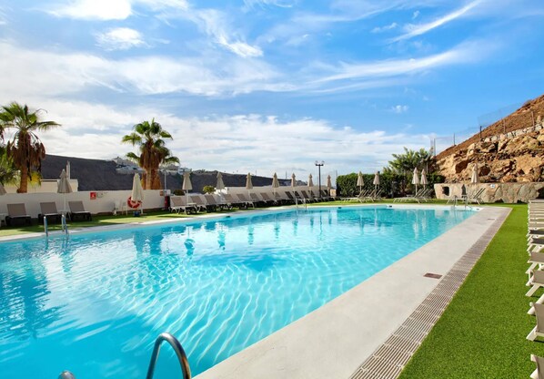 A swimming pool with lounge chairs and palm trees.