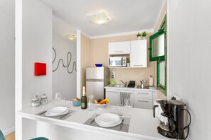 A modern kitchen with white cabinets, a microwave, a coffee maker, and a dining area with a white table set for two.