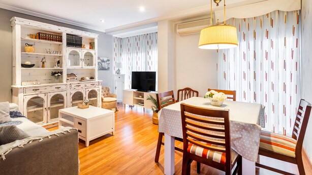 A living room with a dining area, wooden flooring, a white sofa, a TV, and a patterned curtain. - Apartment 'Cristina Center' with Balcony, Wi-Fi and Air Conditioning (València)