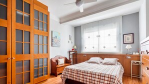 A bedroom with a bed, wooden wardrobe, and a window with curtains. - Apartment 'Cristina Center' with Balcony, Wi-Fi and Air Conditioning (València)
