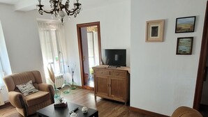 Una sala de estar con sofá, sillón, mesa de centro y televisor sobre un mueble.