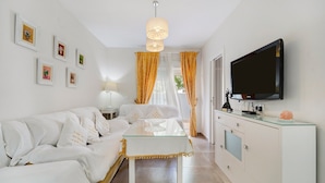 Een moderne woonkamer met een glazen salontafel, een witte bank en een flatscreen televisie aan de muur.